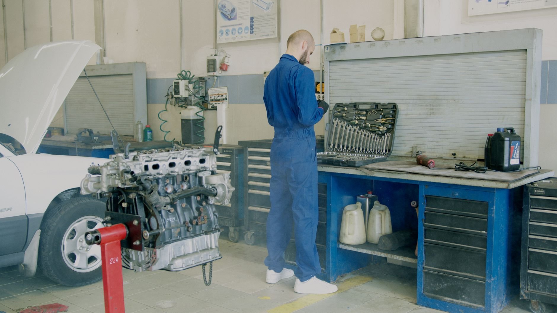 Mechanic in blue coveralls working on car engine in auto repair shop